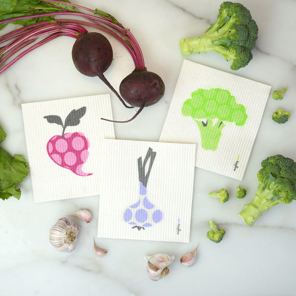 Three Swedish dish clothes with vegetables on them displayed on a table.